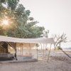 A tented camp setting along the embankment of a river system in Zambia. An open area with dispersed tree vegetation and sand leading towards the river. 