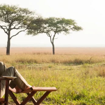 A woman relaxes on outside deck with a drink as she admires the view, Tanzania - Yellow Zebra Safari