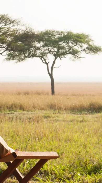 A woman relaxes on outside deck with a drink as she admires the view, Tanzania - Yellow Zebra Safari