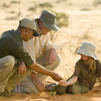 A guide teaches a young girl about tracking whilst sat on the red sand, Tswalu Kalahari, South Africa - Yellow Zebra Safari
