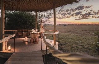 Woman stands on wooden decking watching sunset, Mombo, Moremi Game Reserve, Botswana - Yellow Zebra Safari