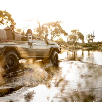 Safari jeep drives through water, Vumbura Plains, Okavango Delta, Botswana - Yellow Zebra Safari