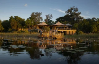 A waterside view of a floating decking and the main lodge which overlooks the water, DumaTau, Botswana - Yellow Zebra Safaris