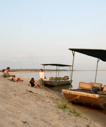 Guests rest on a riverside alongside their parked boats, Tanzania - Yellow Zebra Safari