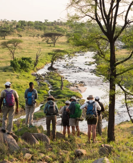 A group of people on walking safari stand above a river as their guide talks - Yellow Zebra Safari
