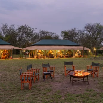 A lit Firepit in the foreground and tented accommodation in the background is lit up in the fading light, Nasikia Mobile Migration Camp, Serengeti, Tanzania - Yellow Zebra Safari