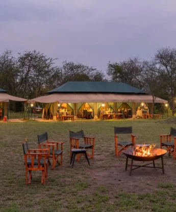 A lit Firepit in the foreground and tented accommodation in the background is lit up in the fading light, Nasikia Mobile Migration Camp, Serengeti, Tanzania - Yellow Zebra Safari
