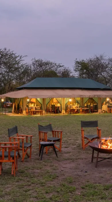 A lit Firepit in the foreground and tented accommodation in the background is lit up in the fading light, Nasikia Mobile Migration Camp, Serengeti, Tanzania - Yellow Zebra Safari