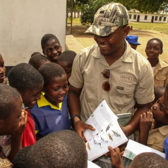 A guide holds a birding book out to a group of children - Yellow Zebra Safaris