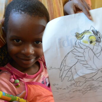 Young child proudly holds up a drawing of an owl - Yellow Zebra Safaris