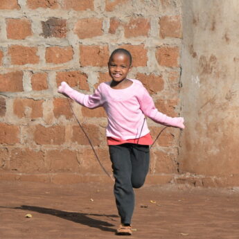 Young girl skips rope and smiles at camera - Yellow Zebra Safaris
