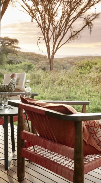 A woman sketches on wooden decking overlooking the reserve, Tanzania - Yellow Zebra Safari