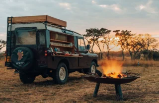 A fire is lit and a safari truck is transformed into a bar ready for Bush Brunch, Wayo Serengeti Green Camp, Tanzania - Yellow Zebra Safari