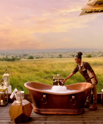 A staff member fills up an outdoor bubble bath on a deck which overlooks the plains, One Nature Mara River, Serengeti, Tanzania - Yellow Zebra Safari