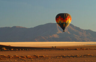 Hot air balloon rises over red dust plains, Wolwedans Plains Camp, Namibia - Yellow Zebra Safaris