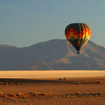 Hot air balloon rises over red dust plains, Wolwedans Plains Camp, Namibia - Yellow Zebra Safaris