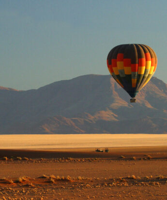 Hot air balloon rises over red dust plains, Wolwedans Plains Camp, Namibia - Yellow Zebra Safaris
