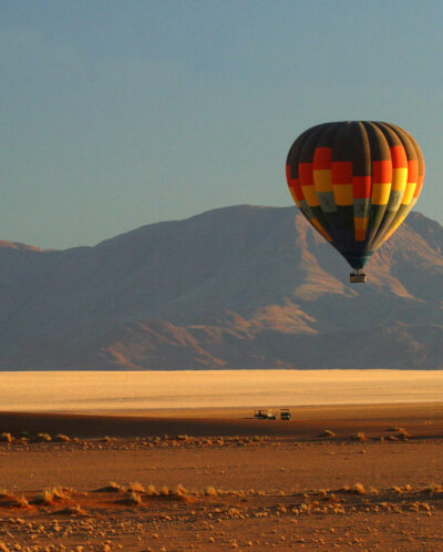 Hot air balloon rises over red dust plains, Wolwedans Plains Camp, Namibia - Yellow Zebra Safaris