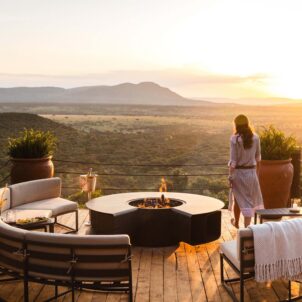A woman stands on a raised wooden deck overlooking the Mara, Cottars Bush Villa, Greater Mara Conservancy, Kenya - Yellow Zebra Safari