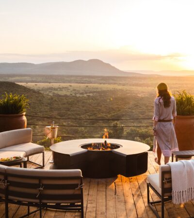 A woman stands on a raised wooden deck overlooking the Mara, Cottars Bush Villa, Greater Mara Conservancy, Kenya - Yellow Zebra Safari