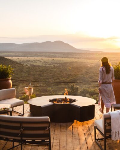 A woman stands on a raised wooden deck overlooking the Mara, Cottars Bush Villa, Greater Mara Conservancy, Kenya - Yellow Zebra Safari