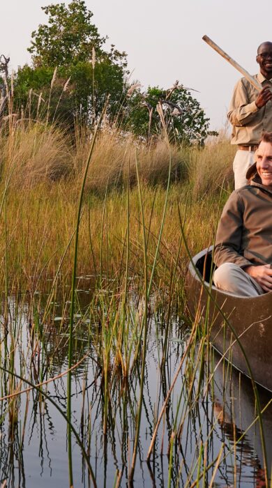A guide steers a Mokoro through the river as a guide sits in the front, Sediba Sa Rona, Moremi Game Reserve, Botswana - Yellow Zebra Safari